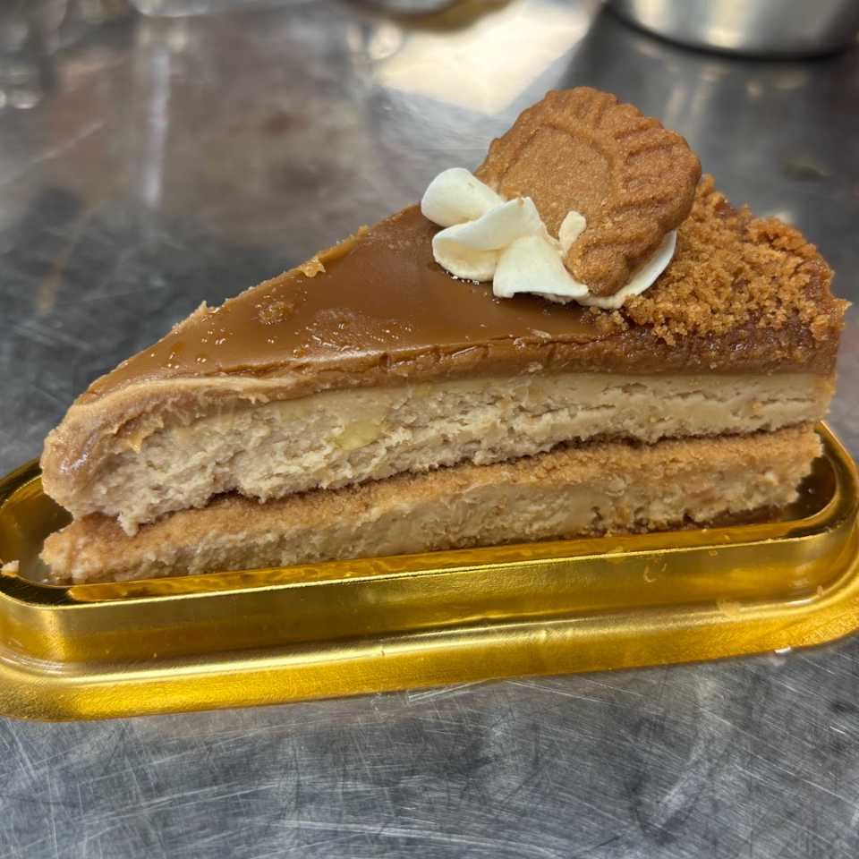 Slice of layered caramel cheesecake topped with whipped cream and a cookie on a gold serving tray.
