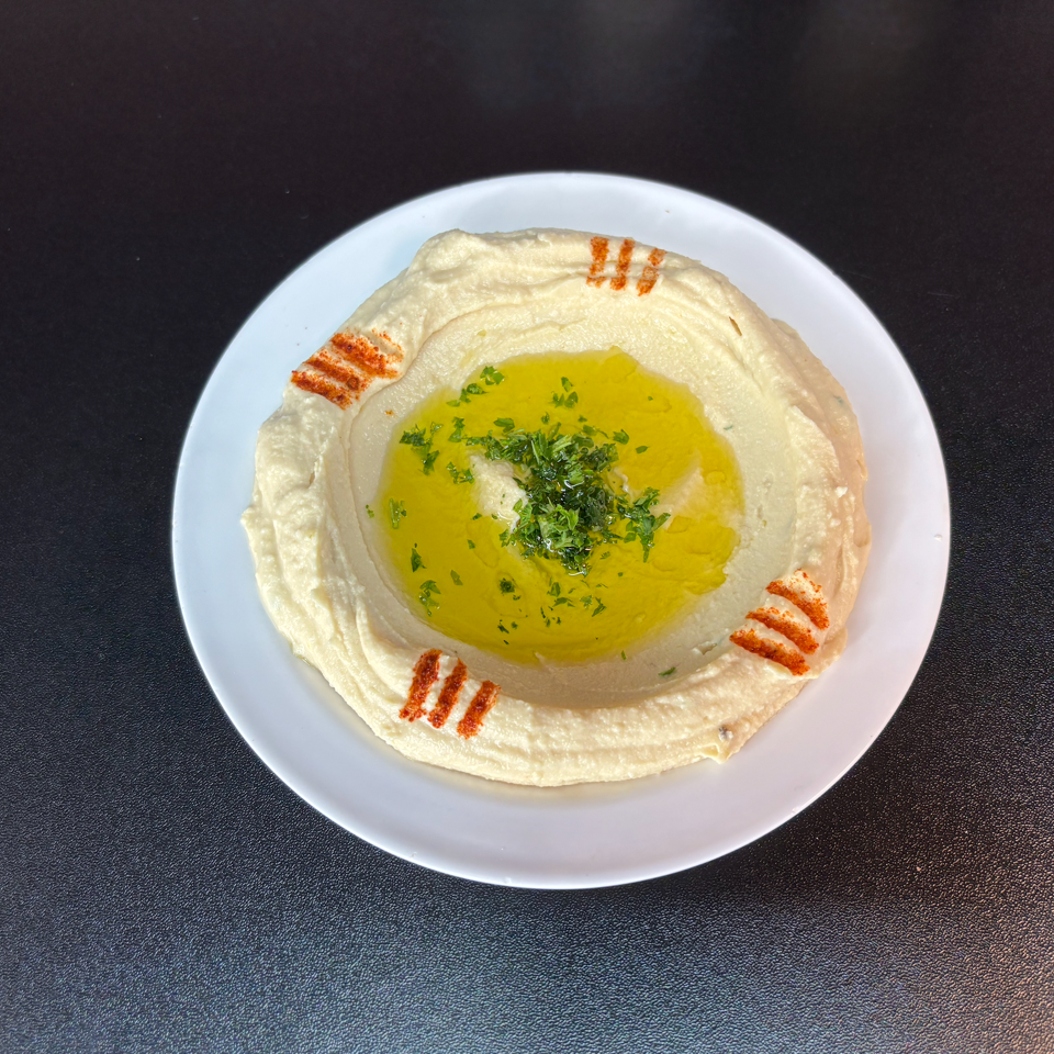 Plate of hummus topped with olive oil, chopped parsley, and paprika on a dark tabletop.